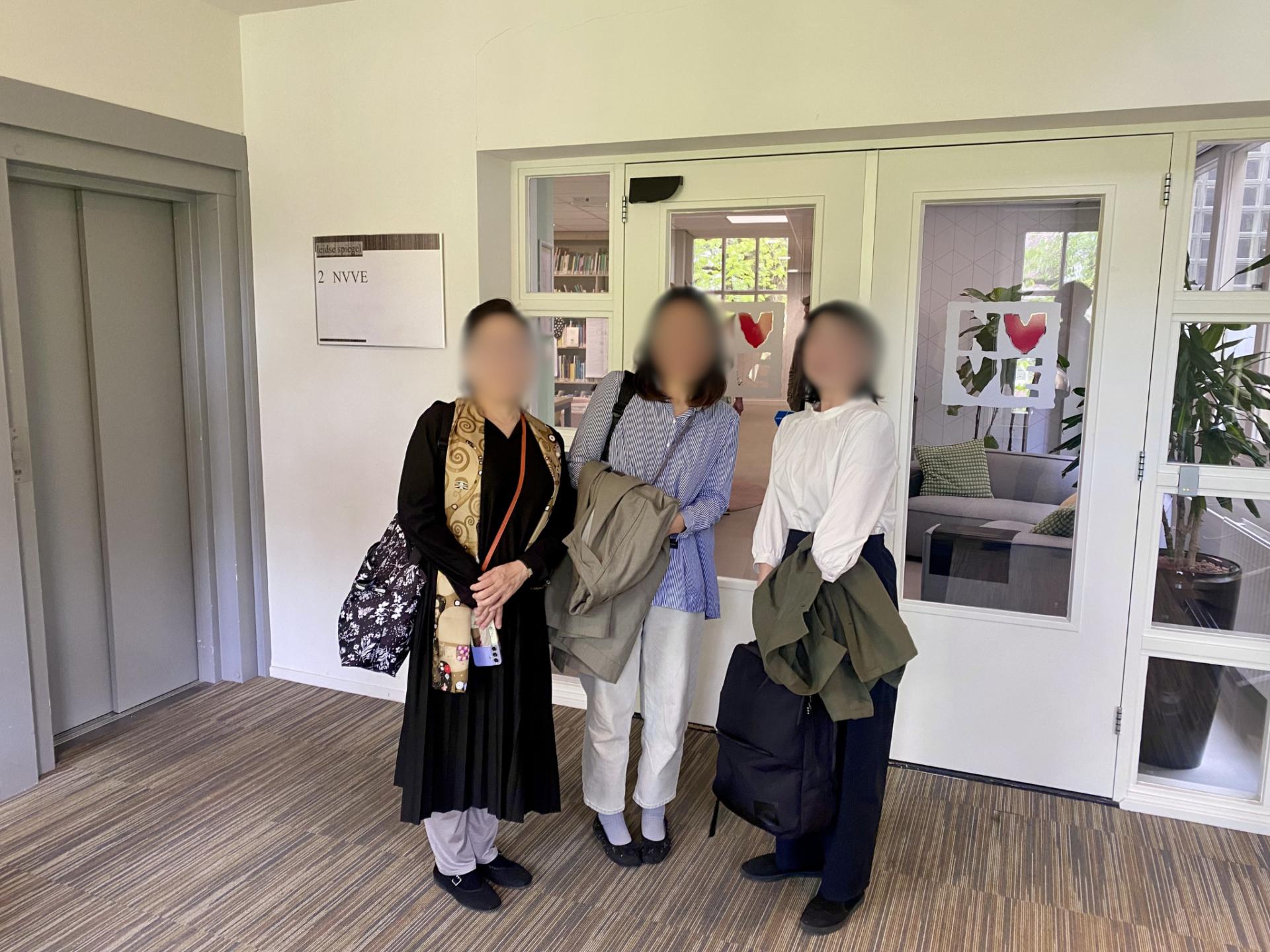 NVVEの表札が見える入口前での記念写真。元の顔ぼかしを保持。